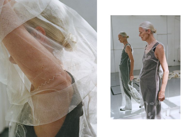 Fashionable elderly female model in an artful photo. She poses in a sheer layered dress with a side profile and reflections in a bright indoor studio.