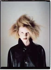 Model Lexy Hearn with voluminous teased hair wearing a black leather jacket against a neutral studio backdrop.