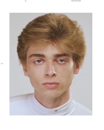 Close-up portrait of model Luka Hoogedeure with textured blonde-brown hair wearing a white mock-neck top against a light grey background.
