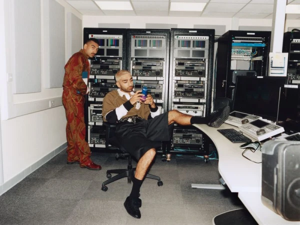 Mawaan and Nabhaan Rizwan styled in designer streetwear inside an audio broadcast control room with equipment racks.