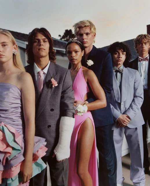 Group of young adults in formal wear, lined up outdoors. One person has a cast on their arm. Prom or fashion editorial aesthetic.