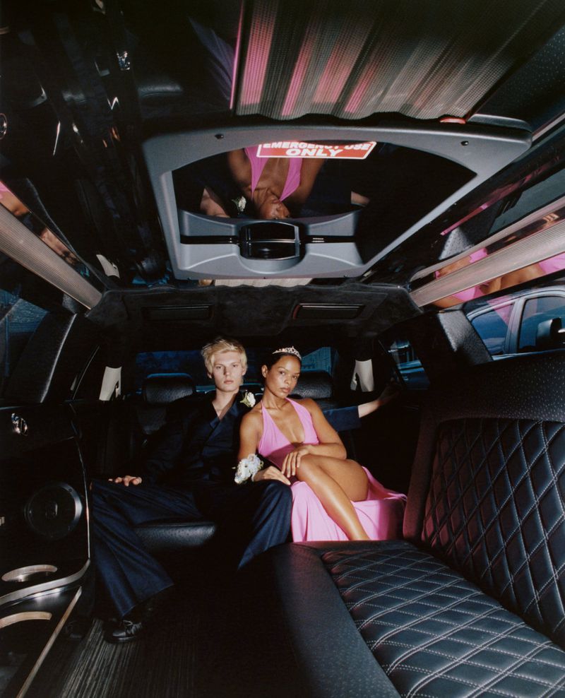 Teenage couple in a black limousine. The woman in a pink dress and tiara sits next to the young man in a suit. Formal event fashion.