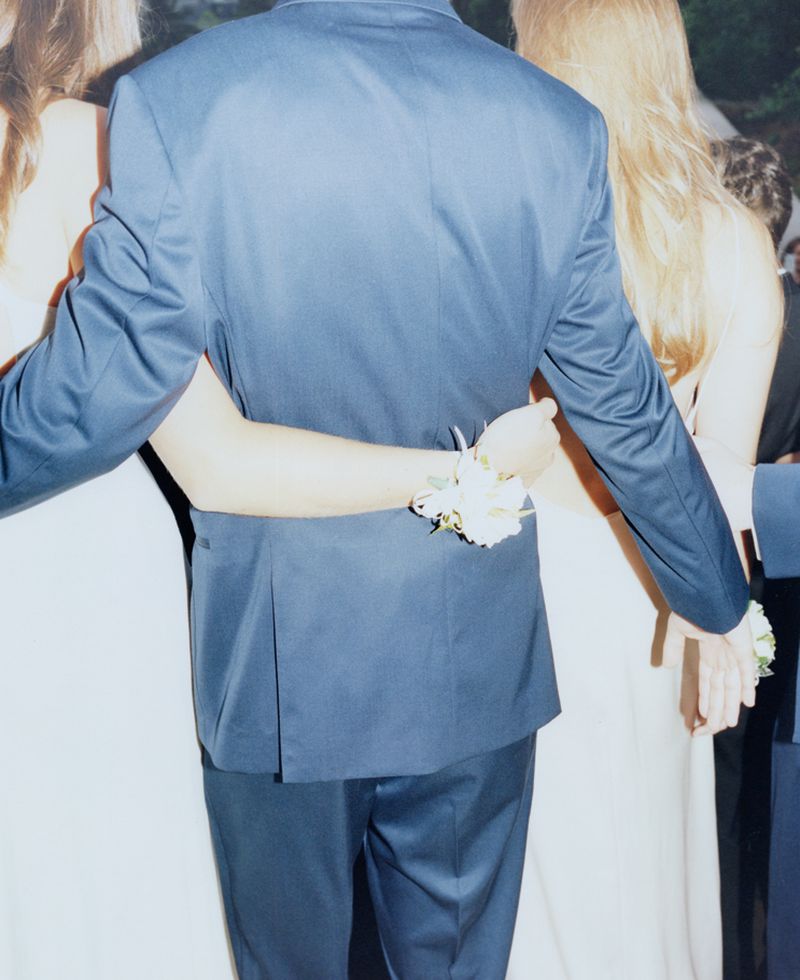 Back view of a prom couple in formalwear, with flower wrist corsage and hug; group of people; celebration; dance party; formal dance.