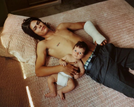 Adult male with cast on arm and baby lying on bed, medium shot, indoor setting, warm lighting, casual attire, portrait photography.