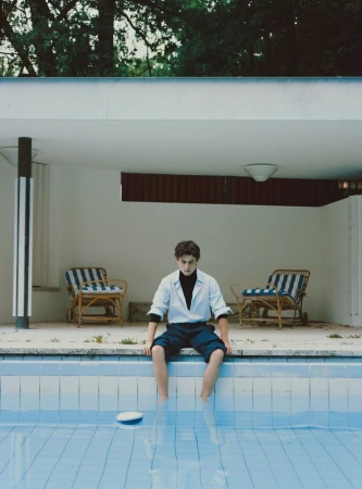 Julien de Saint Jean sits on the edge of a tiled outdoor swimming pool wearing a light blue shirt over a black top and dark shorts.