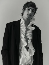 Model Silas Lutz Fabian in a black blazer and white ruffled collar against a studio background.