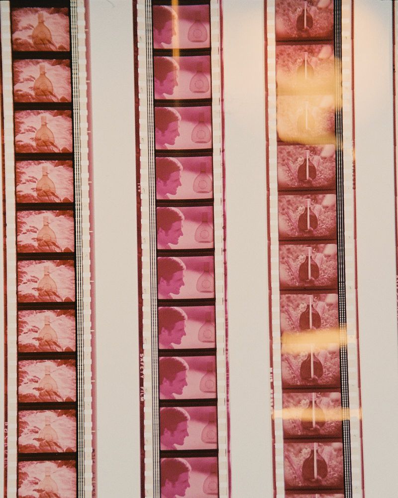 Film strips show vintage images of a man's profile and an object resembling a bottle with light orange and pink color grading.