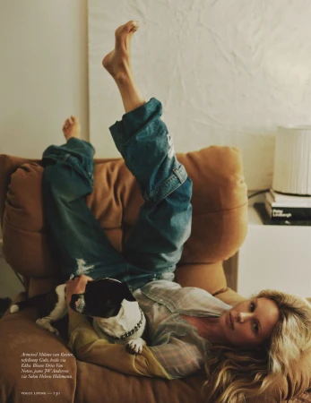 Model Marlijn Hoek lounges upside down on a brown armchair with bare feet raised, holding a small dog on her chest.