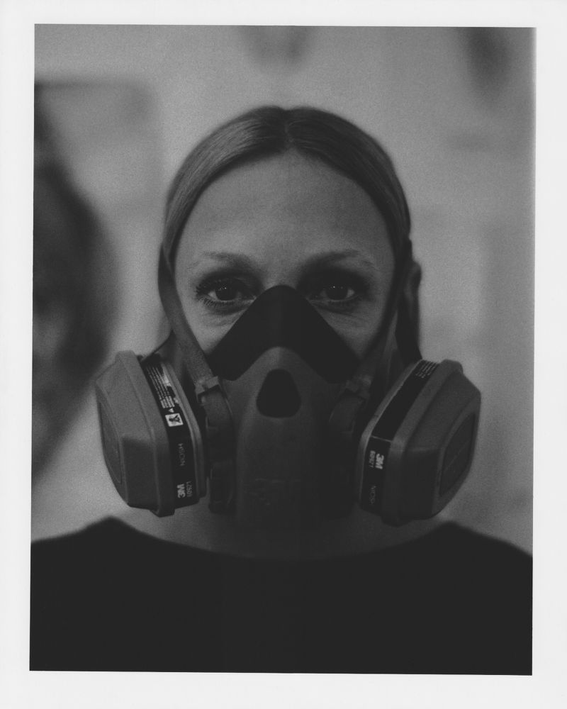 Monochrome portrait of an adult female wearing a respirator mask against a blurred background in a photo studio setting.