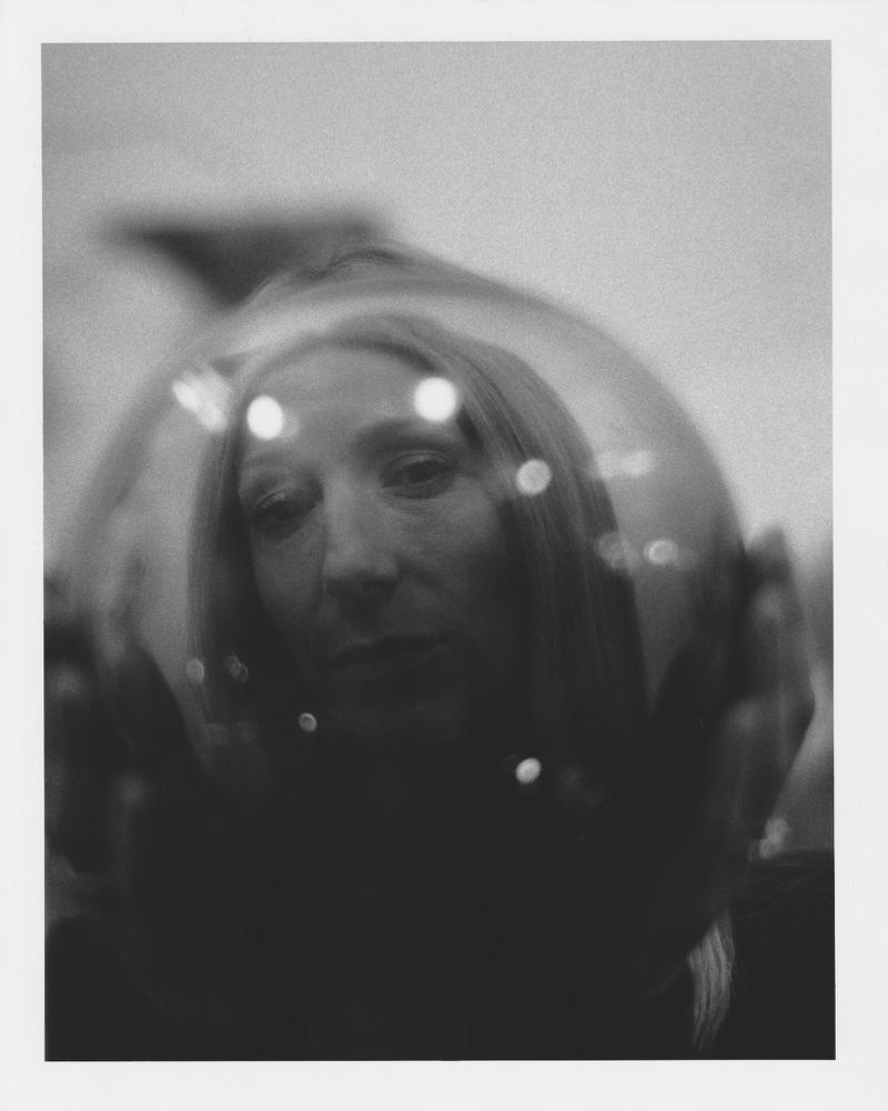 Portrait of a woman in black and white with a fishbowl over her head, soft focus, indoors.