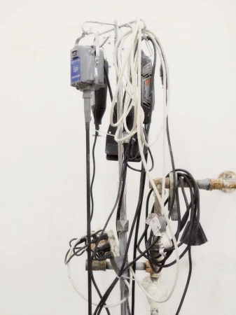 Close-up of multiple power tools hanging from a metal stand against a white wall, featuring coiled cords and attached hoses.