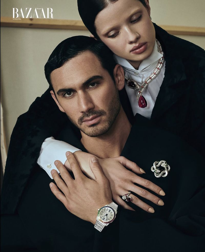 Editorial shot of a couple posing indoors, wearing fine jewelry and dark attire, with a 'BAZAAR' logo in the upper left.