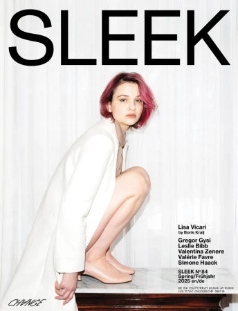 Lisa Vicari squatting on a marble surface in a white coat with pink hair for Sleek Magazine