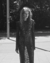 Model with long wavy hair standing outdoors in a sheer black knit long-sleeved dress in black and white.
