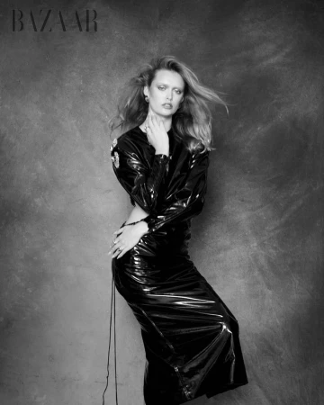 Model Erin Cromwell poses in a glossy black vinyl dress against a textured studio backdrop for Harper's Bazaar Vietnam.