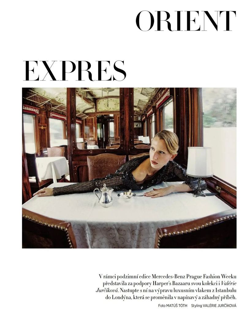 Fashion shot inside Orient Express train car: blond model poses at table with tea service, dark sequined top, editorial, travel.