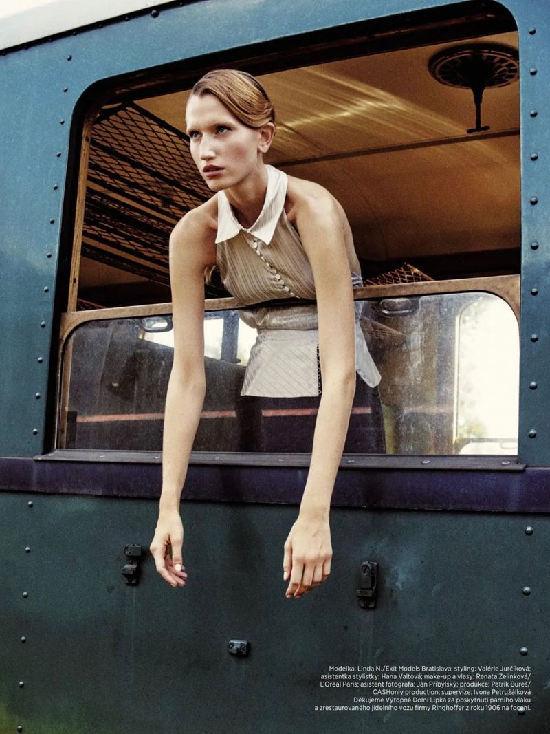 A woman with her arms hanging out of a vintage train window is the primary focus, exhibiting a fashion editorial style and neutral color palette.