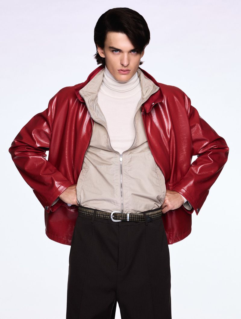 Male model wearing a red leather jacket, neutral zip-up jacket, black trousers, and patterned belt against a clean white backdrop.