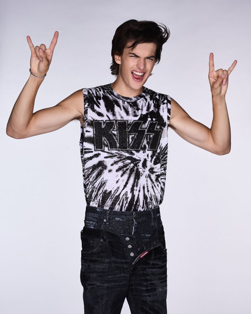 Young adult posing with rock-on hand gestures, wearing a black and white KISS t-shirt and designer black jeans against a white backdrop.