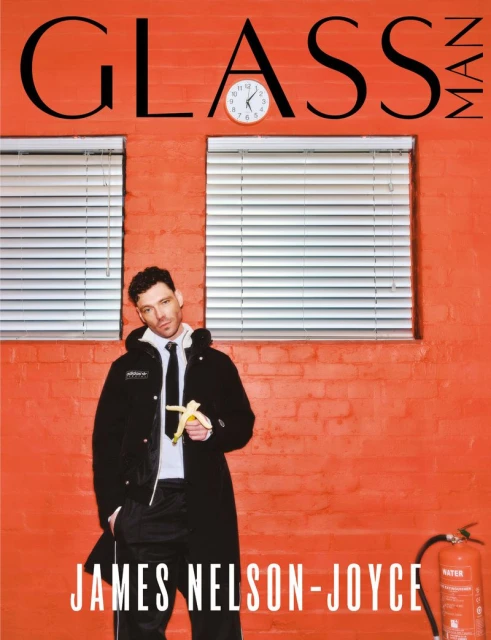 Magazine cover featuring James Nelson-Joyce in a black coat holding a banana, with red brick wall, white blinds, and "GLASS MAN" text.