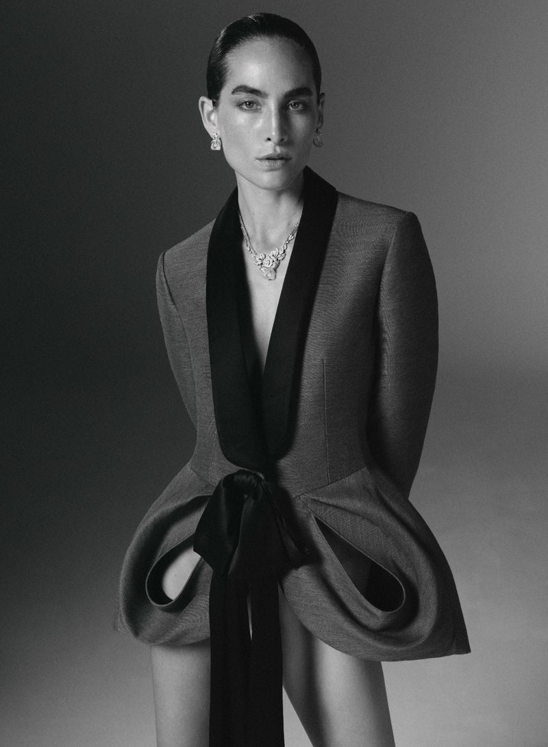 Model Heather Kemesky wearing a sculptural tailored jacket with draped hips and a diamond necklace against a studio backdrop.