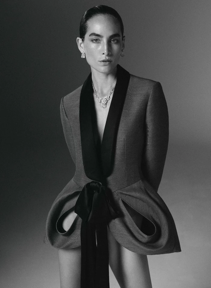 Model Heather Kemesky wearing a sculptural tailored jacket with draped hips and a diamond necklace against a studio backdrop.