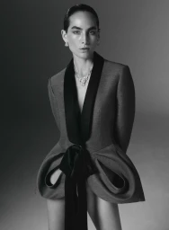 Model Heather Kemesky wearing a sculptural tailored jacket with draped hips and a diamond necklace against a studio backdrop.
