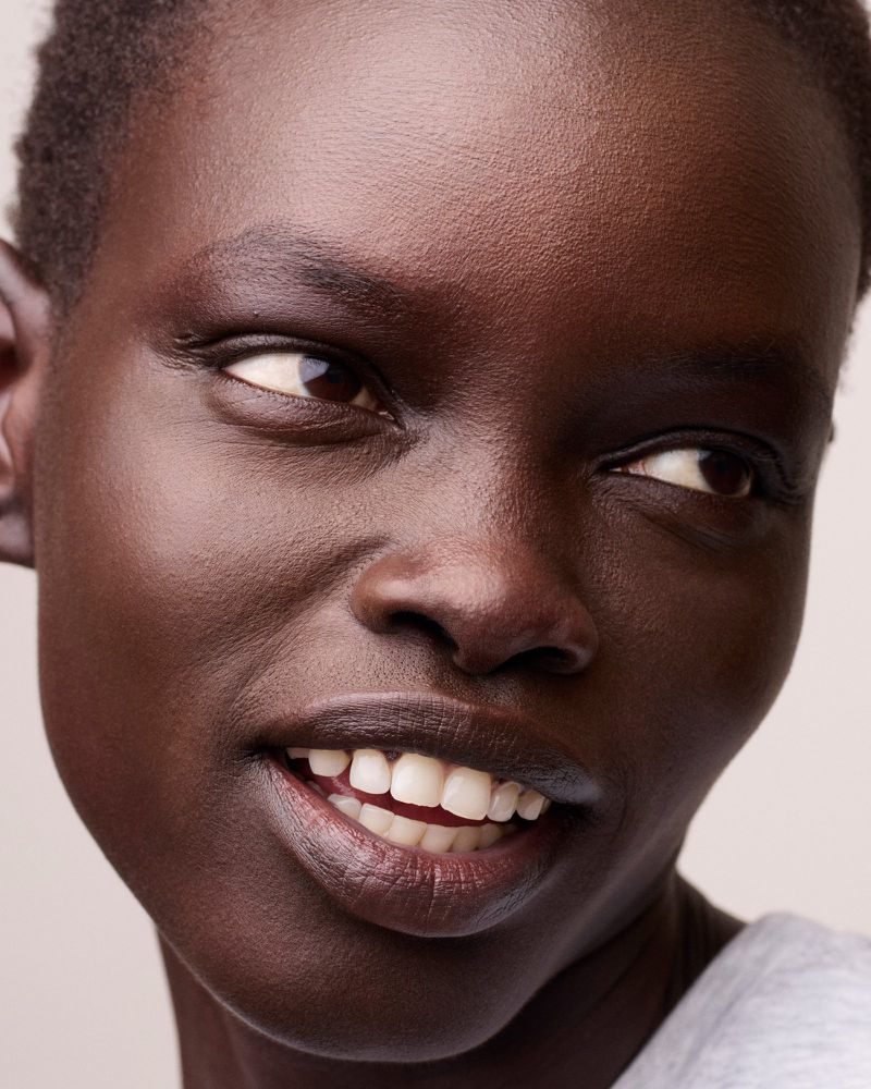 Close-up portrait of a smiling African-American woman, focusing on her radiant complexion and genuine expression in a soft, neutral setting.