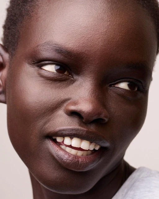 Close-up portrait of a smiling African-American woman, focusing on her radiant complexion and genuine expression in a soft, neutral setting.