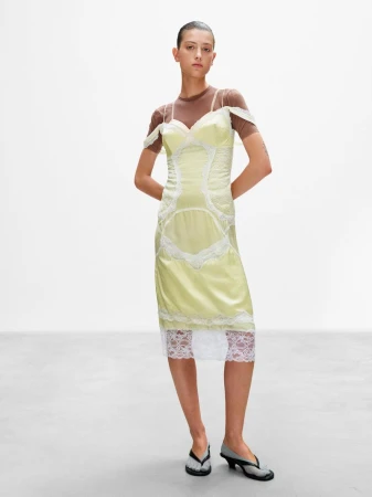 Model in pale yellow lace-trimmed slip dress and brown top against a white studio background