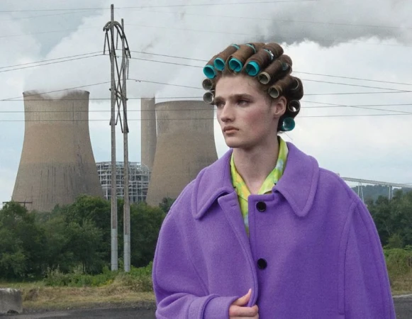 Model in a purple coat and hair rollers with large industrial cooling towers in the background for Double Magazine