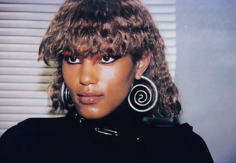 Portrait of a stylish adult female with unique spiral earrings and dramatic makeup indoors, showcasing beauty and fashion.