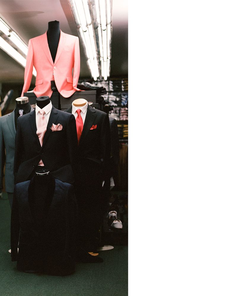 Retail display of men's formal wear featuring mannequins dressed in suits and ties, under fluorescent lighting in a shop.