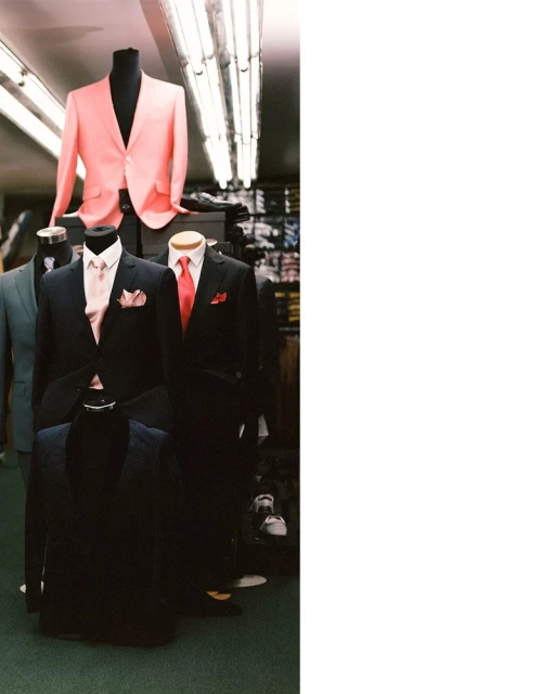 Retail display of men's formal wear featuring mannequins dressed in suits and ties, under fluorescent lighting in a shop.