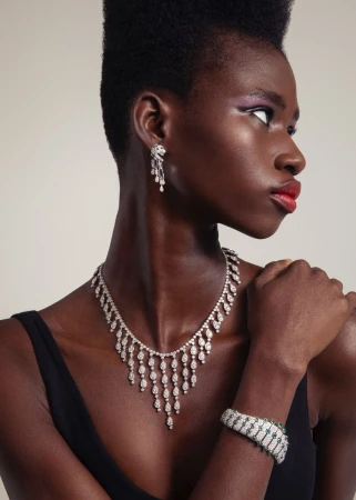 Black woman wearing a diamond fringe necklace, matching earrings, and a bracelet in profile against a neutral studio backdrop.