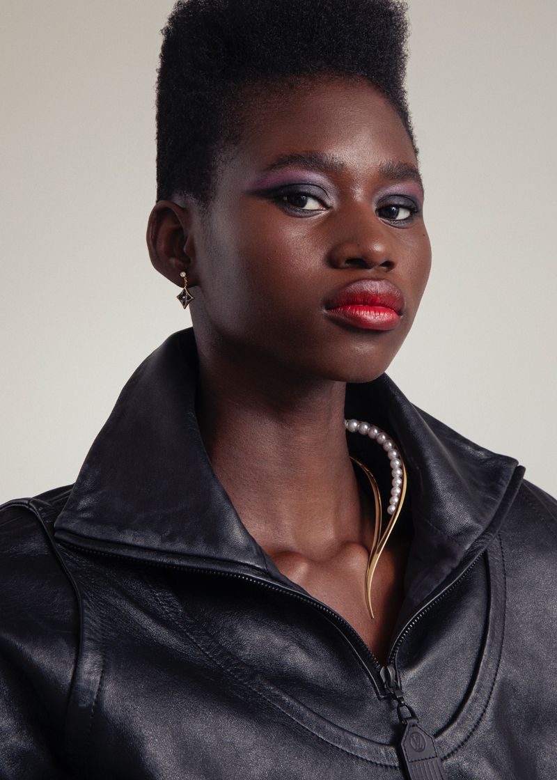 Close-up portrait of a young Black woman with dark hair and purple eyeshadow wearing a black leather jacket and a pearl necklace. 