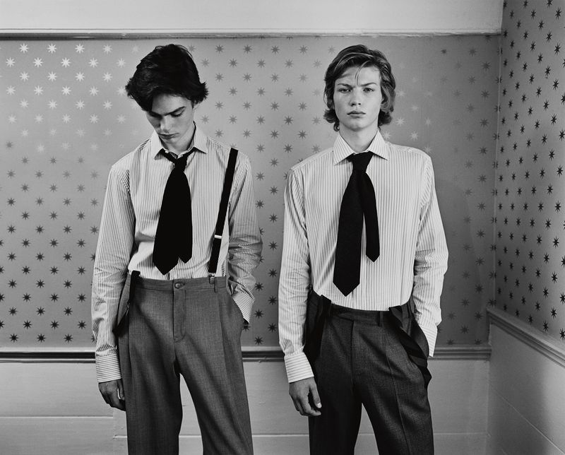 Two young adult men in a photo studio wearing ties and suspenders, posing against a star-patterned wall, creating a vintage fashion look.