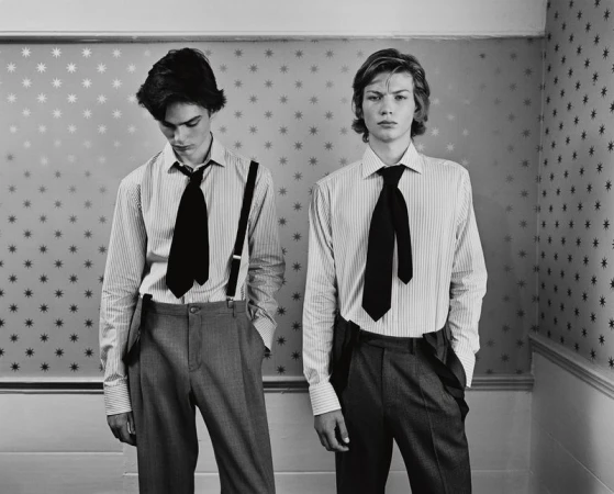 Two young adult men in a photo studio wearing ties and suspenders, posing against a star-patterned wall, creating a vintage fashion look.