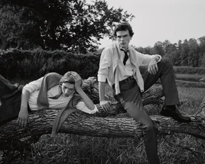 Two young male models in white shirts posing outdoors on a fallen tree trunk in a monochrome editorial photograph