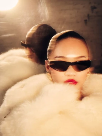 Suni Lee wearing black sunglasses and a white fur coat with a reflection visible in a mirror behind her.