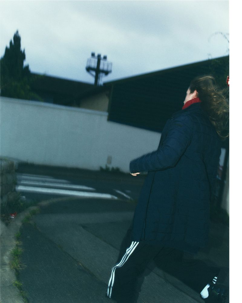 Adult walks across a zebra crossing in an urban setting wearing a dark jacket and black pants with white stripes on the side.