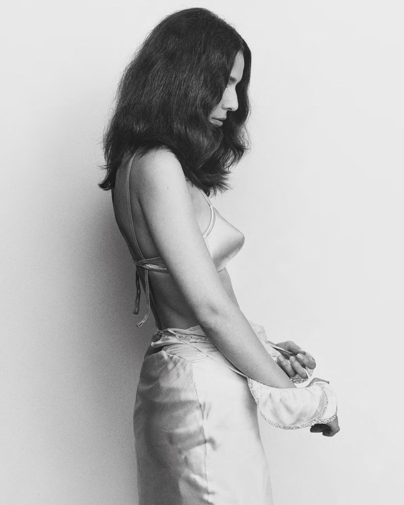 Black and white portrait of a woman with medium length dark hair wearing a satin skirt and halter top against a light background.