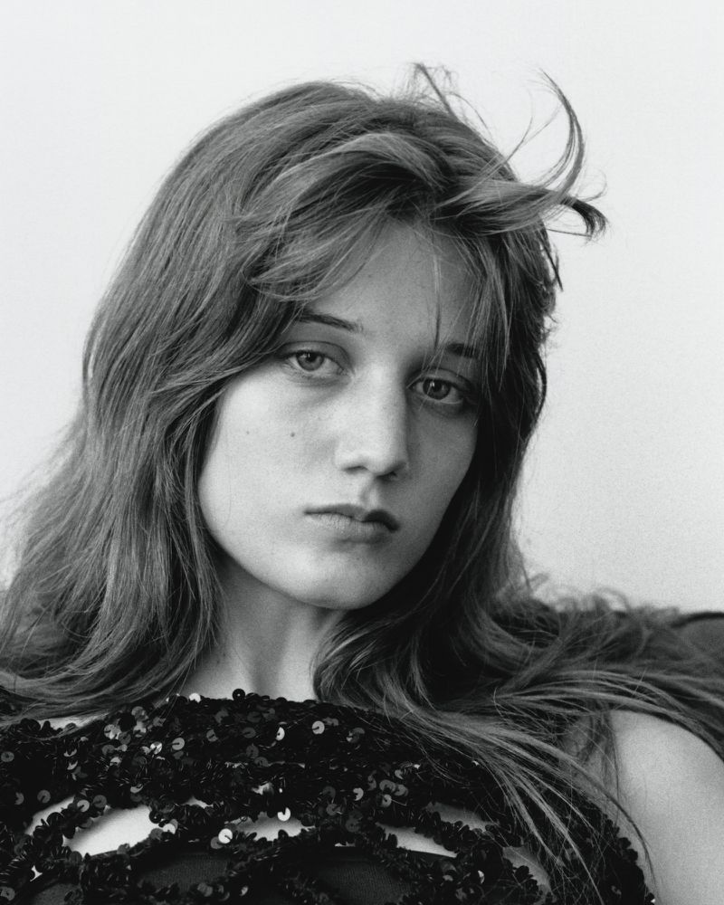 Portrait of a young woman with long dark hair wearing a black sequin top against a plain light background