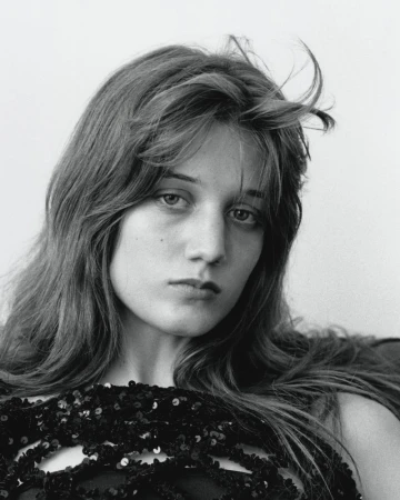 Portrait of a young woman with long dark hair wearing a black sequin top against a plain light background