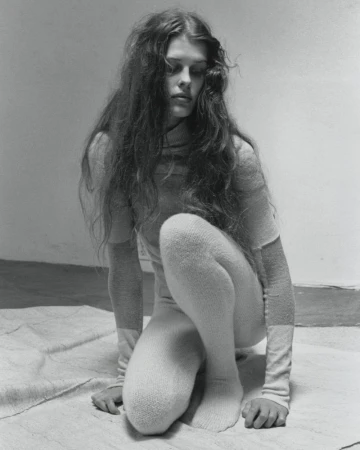 Black and white portrait of a female model crouching on a draped canvas surface in a minimalist studio.
