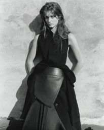 Monochrome fashion portrait of a model leaning against a textured concrete wall wearing a dark sleeveless top