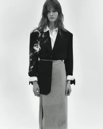 Monochrome portrait of a female model wearing a structured black blazer with white textural embellishments over a white shirt and skirt.