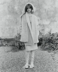 Fashion model wearing an oversized hooded wrap coat and skirt on a gravel ground in black and white.