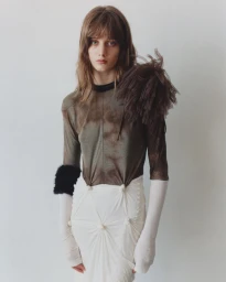 Model in grey long-sleeve top and white pleated skirt against a plain wall