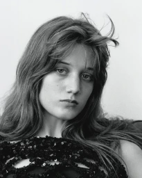 Portrait of a young woman with long dark hair wearing a black sequin top against a plain light background
